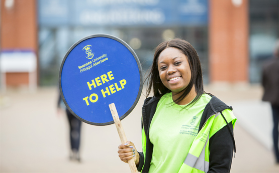 Student at an open day holding a here to help sign